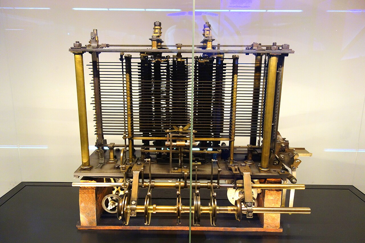 Modelo experimental parcial da Máquina Analítica, com colunas de engrenagens e estrutura metálica, exposto em vitrine.